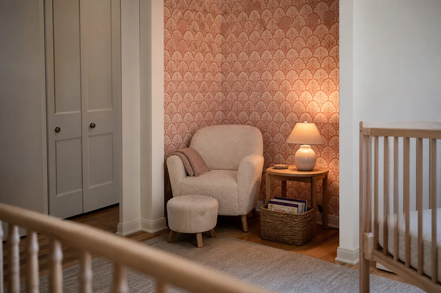 Pink nursery wallpaper accent wall beside a cozy reading chair