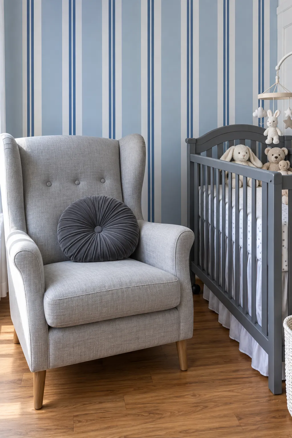 Nursery scheme pairing blue striped walls with a gray armchair and gray crib.